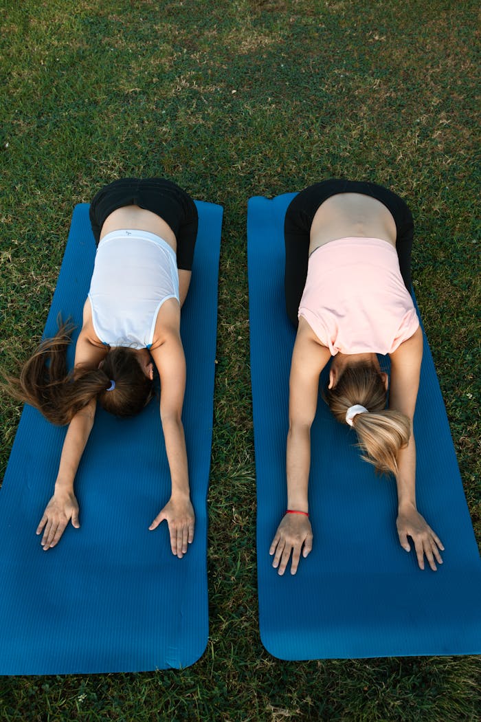 who-we-are Two women performing yoga poses on mats outdoors, emphasizing fitness and tranquility.